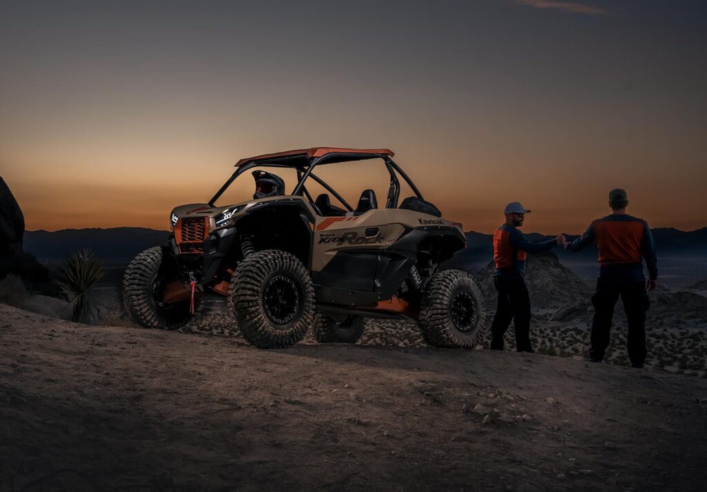 Two people standing beside a sport side-by-side on a desert ridge at sunset