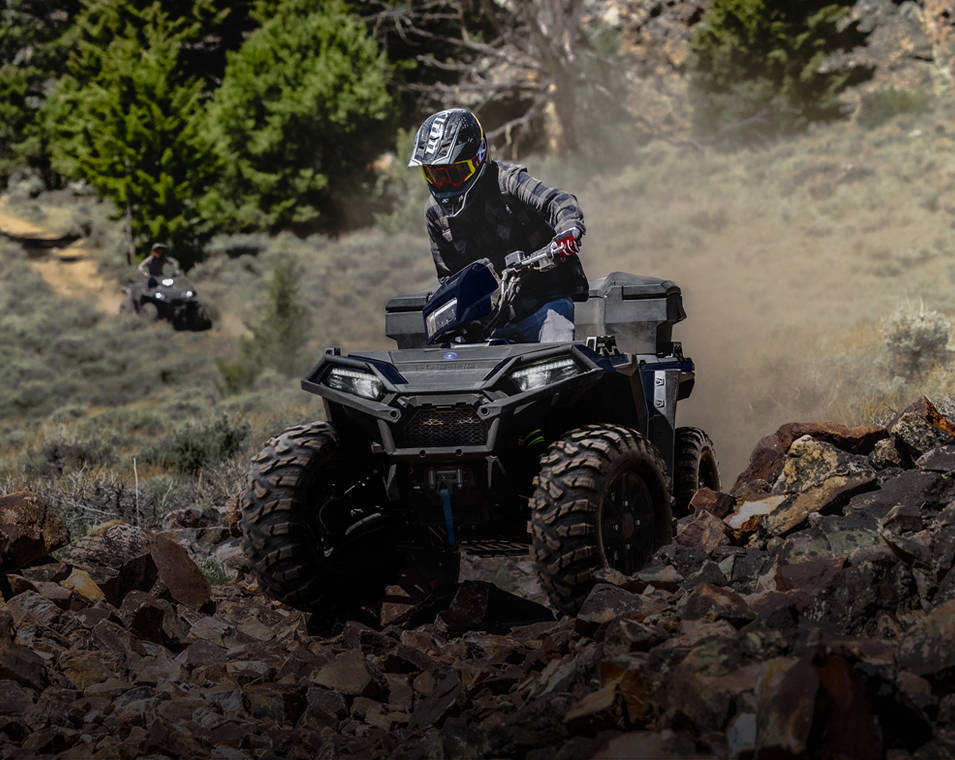 Rider powering a Polaris Sportsman utility ATV through mud and trees