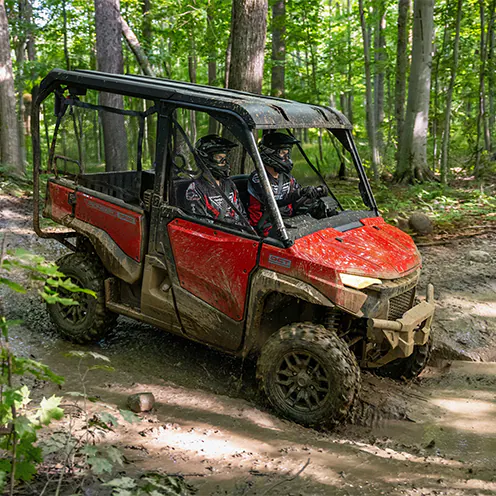 Red Honda Pioneer utility side-by-side carrying two riders on a wooded trail